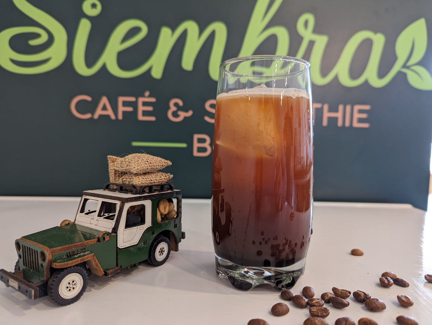 Premium Colombian coffee beans from Pitalito, Huila. Chocolate and nutty notes. Fair trade, hand-harvested, artisan roasted in Montreal.
Black coffee bag on a wooden table with a cup of coffee in a kitchen setting
Glass of iced coffee with a toy jeep and coffee beans on a table with 'Siembra' background
